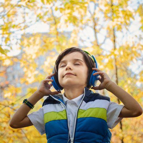 Boy enjoying music with headphones in a colorful autumn setting.