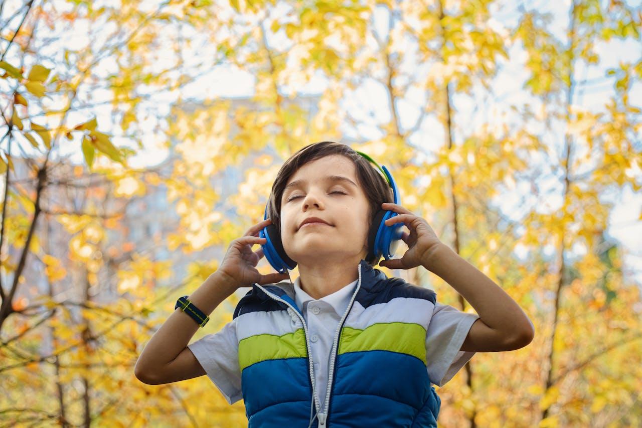 Boy enjoying music with headphones in a colorful autumn setting.