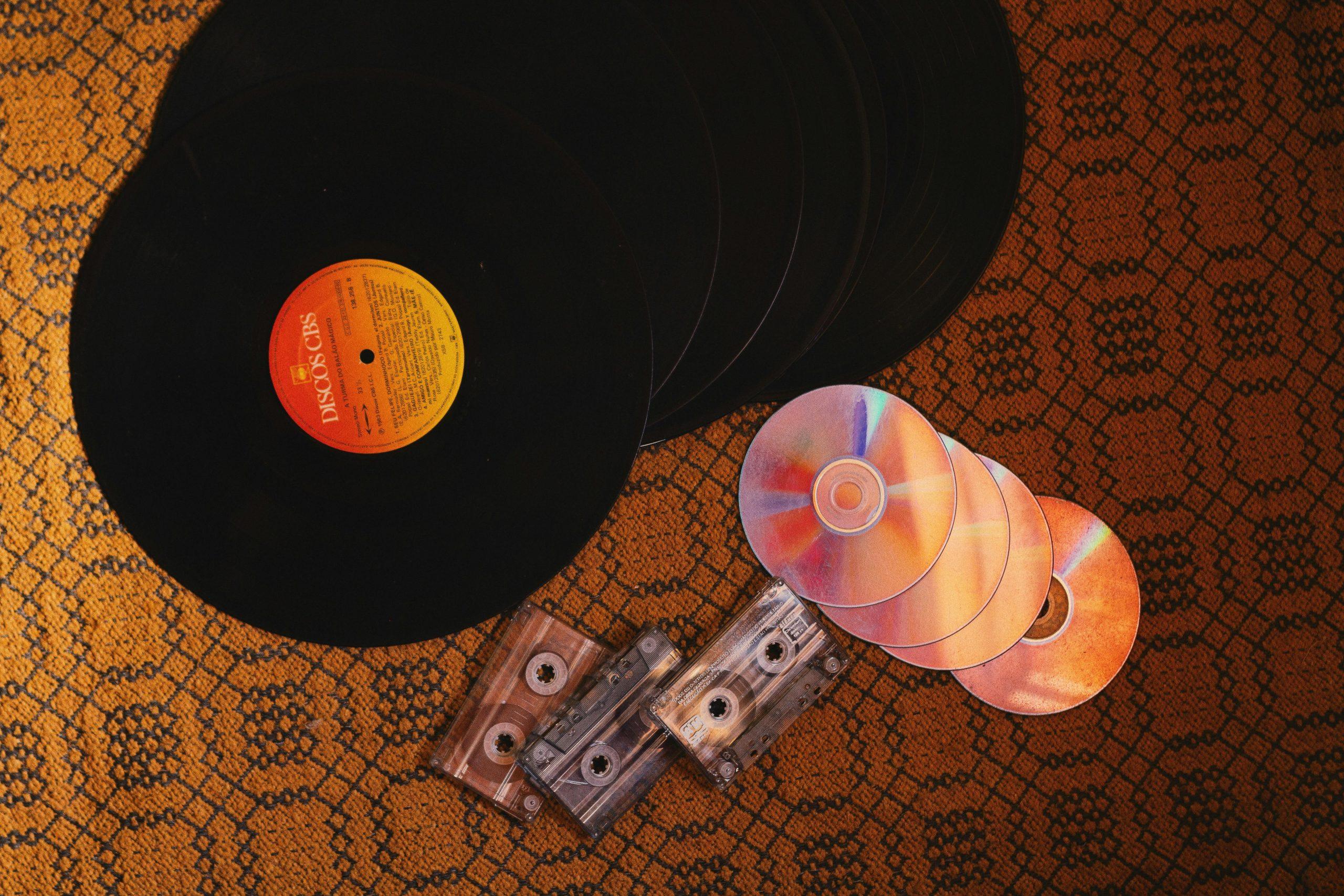 "Vinyl records, cassette tapes, and CDs on a patterned surface."